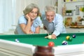 Happy senior couple playing billiards together in home