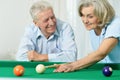 Happy senior couple playing billiards together in home