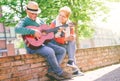 Happy senior couple playing a guitar while sitting outside on a wall on a sunny day Royalty Free Stock Photo