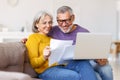 Happy senior couple reading good news in letter while paying bills online on laptop