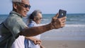 Senior couple relaxing outdoors walking on the sea shore and taking selfie together with smartphone on the beach Royalty Free Stock Photo