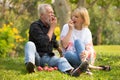 Happy senior couple relaxing in park eating apple together morning time. old people sitting on grass in the autumn park . Elderly