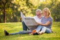 Happy senior couple relaxing in park reading newspaper together . old people sitting on grass in the summer park . Elderly resting