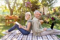 Happy senior couple resting on picnic blanket in garden, man using laptop computer, woman reading book Royalty Free Stock Photo