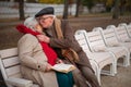 Happy senior couple sitting on bench and hugging outdoors in town park in autumn. Royalty Free Stock Photo