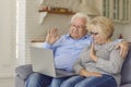 Happy senior couple sitting on comfy sofa, video calling family and waving hands at laptop screen Royalty Free Stock Photo