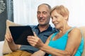 Happy senior couple sitting on couch and using digital tablet Royalty Free Stock Photo