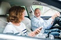 Happy senior couple with smartphone sitting in car, going on trip.