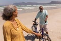 Senior couple standing with bicycle and looking each other on beach with mountains in the back Royalty Free Stock Photo