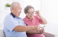 Happy senior couple using cell phone together at home, surfing internet, sitting on couch Royalty Free Stock Photo