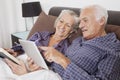 Happy senior couple using digital tablet while lying on bed in room Royalty Free Stock Photo