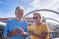 Happy senior couple walking on a bridge in the city. Looking at their own mobile phone and smiling. Elderly modern and