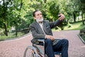 Happy senior disabled or handicapped bearded man sitting on a wheelchair in park, using his smartphone for photographing Royalty Free Stock Photo