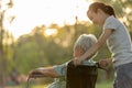 Happy senior disabled woman in wheelchair with granddaughter walking outside at park on sunny day,smiling child girl and elderly Royalty Free Stock Photo