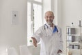 Happy senior doctor reaching out for handshake, welcoming new patient into his medical office. Royalty Free Stock Photo