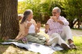 Happy senior european man and woman eat sandwiches, drink coffee takeaway, enjoy romantic date, lunch in park Royalty Free Stock Photo