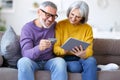Happy senior family couple paying bills online with credit card, using digital tablet for shopping Royalty Free Stock Photo