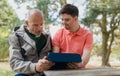 Happy senior father with his young son with Down syndrome using tablet and sitting in park. Royalty Free Stock Photo