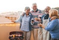 Happy senior friends having fun cheering with red wine at barbecue on terrace - Mature people dining and laughing together at bbq Royalty Free Stock Photo