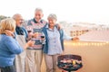 Happy senior friends having fun drinking red wine at barbecue dinner in terrace - Mature people dining and laughing together Royalty Free Stock Photo