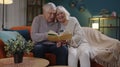 Senior grandparents couple relaxing, reading book, talking enjoying leisure hobbies at night home Royalty Free Stock Photo