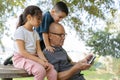 Happy senior grandfather using smart phone while grandson looks over his head, granddaughter sitting near. Royalty Free Stock Photo