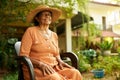 Happy senior Indian woman sitting in chair in the garden of her house smiling looking at camera. Elderly retired Sri Royalty Free Stock Photo