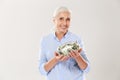 Happy senior lady in blue shirt holding glass bank with dollars, looking at camera Royalty Free Stock Photo