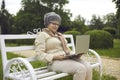 Happy senior lady using laptop sitting on bench relaxing in park outdoors