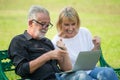 Happy senior loving couple relaxing with laptop computer at park excited together in morning time. old people sitting on a bench