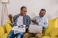 happy senior man and adult son reading business newspaper and using laptop on sofa Royalty Free Stock Photo