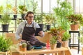 Senior man gardening wearing glasses and denim apron with digital tablet sitting in home gardening for looking who buys the tree. Royalty Free Stock Photo