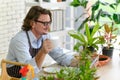 Happy senior man gardening wearing glasses and denim apron sitting and drinking coffee while reading newspaper in his home Royalty Free Stock Photo