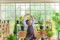 Happy senior man gardening wearing glasses and denim apron sitting in home gardening and stretching his arms, pulls hands up Royalty Free Stock Photo