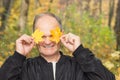 Happy senior man Holding and covering her eyes with two yellow maple leaves in the autumn city park. Active seniors. Royalty Free Stock Photo