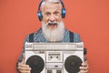 Happy senior man listening to music with boombox and headphones outdoor - Crazy hipster male having fun with vintage stereo