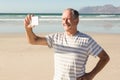 Happy senior man photographing through mobile phone at beach Royalty Free Stock Photo