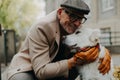 Happy senior man sitting on bench and embracing his dog outdoors in park in city. Royalty Free Stock Photo