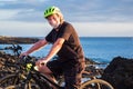 Happy senior man standing on the cliff riding his bici and looking at camera.Two electric bicycle close to him. Blue ocean water Royalty Free Stock Photo