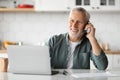 Happy Senior Man Talking On Cellphone And Using Laptop In Kitchen Royalty Free Stock Photo