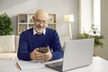 Happy senior man using his mobile phone while sitting at desk with laptop computer Royalty Free Stock Photo