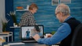 Happy senior man waving during video conference with nephews using laptop