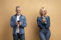 Happy senior man and woman using cell phones, beige background Royalty Free Stock Photo