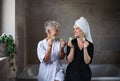 Happy senior mother in bathrobe with adult daughter indoors at home, selfcare concept.