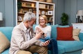 Happy senior old couple holding smartphone looking at cellphone screen laughing relaxing sit on sofa together, smiling elder