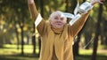 Happy senior old lady throwing stack of dollar bills in park, planned retirement Royalty Free Stock Photo