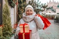 Happy senior 50s blonde woman having fun holding shopping bag full of Christmas gift boxes on city street. Seasonal Royalty Free Stock Photo