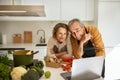 Happy senior spouses watching video recipe on laptop while cooking lunch in kitchen interior together, free space Royalty Free Stock Photo