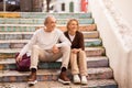 Happy Senior Tourists Couple Sitting On Colorful Steps Outdoors