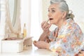 Happy senior woman applying makeup near dressing table Royalty Free Stock Photo